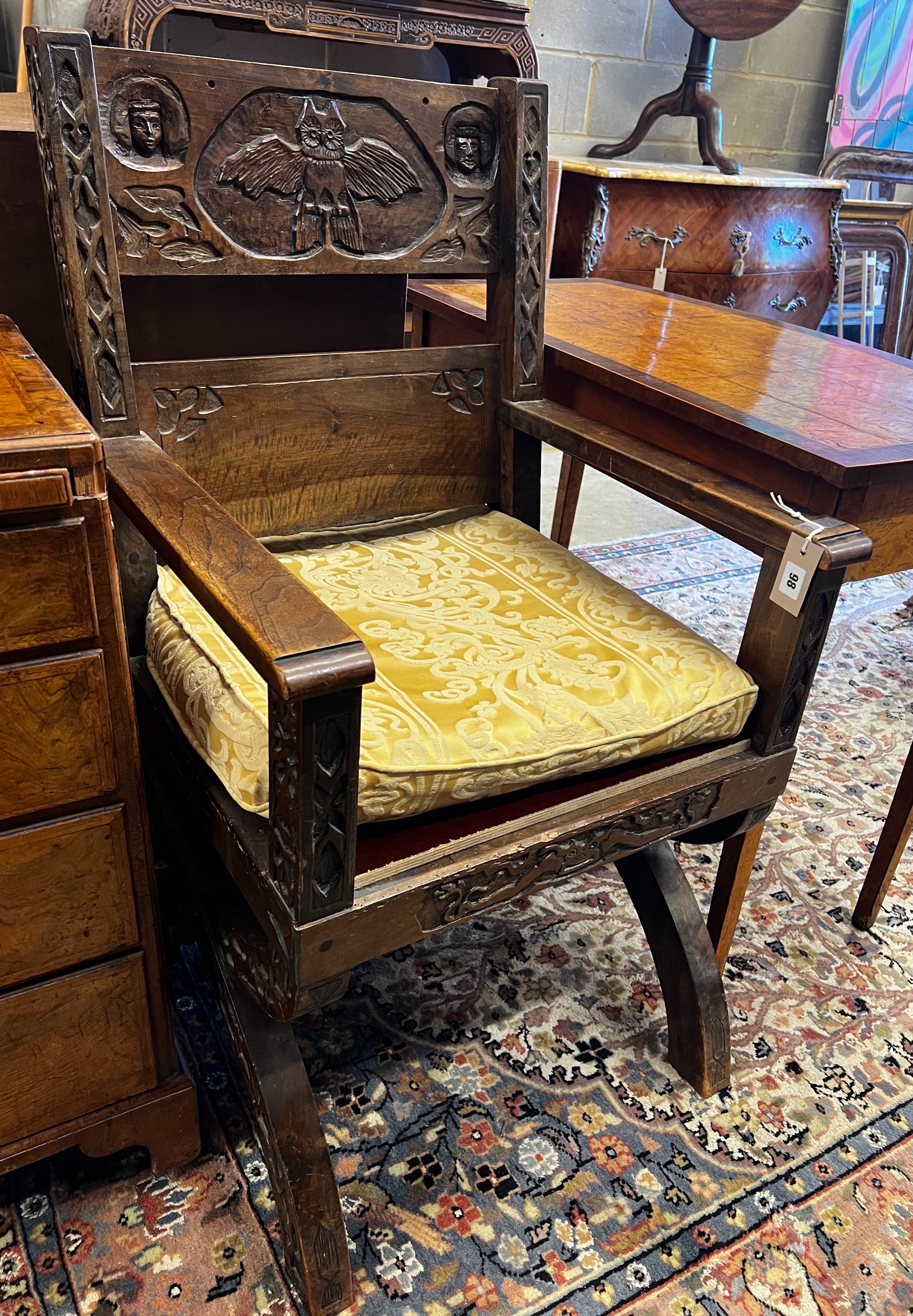 A 17th century style carved oak X-frame elbow chair with carved owl and figural motifs, width 58cm, depth 50cm, height 105cm